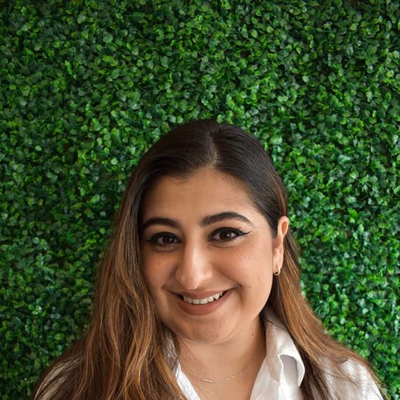 Kimya smiling in a white blouse against a verdant backdrop.