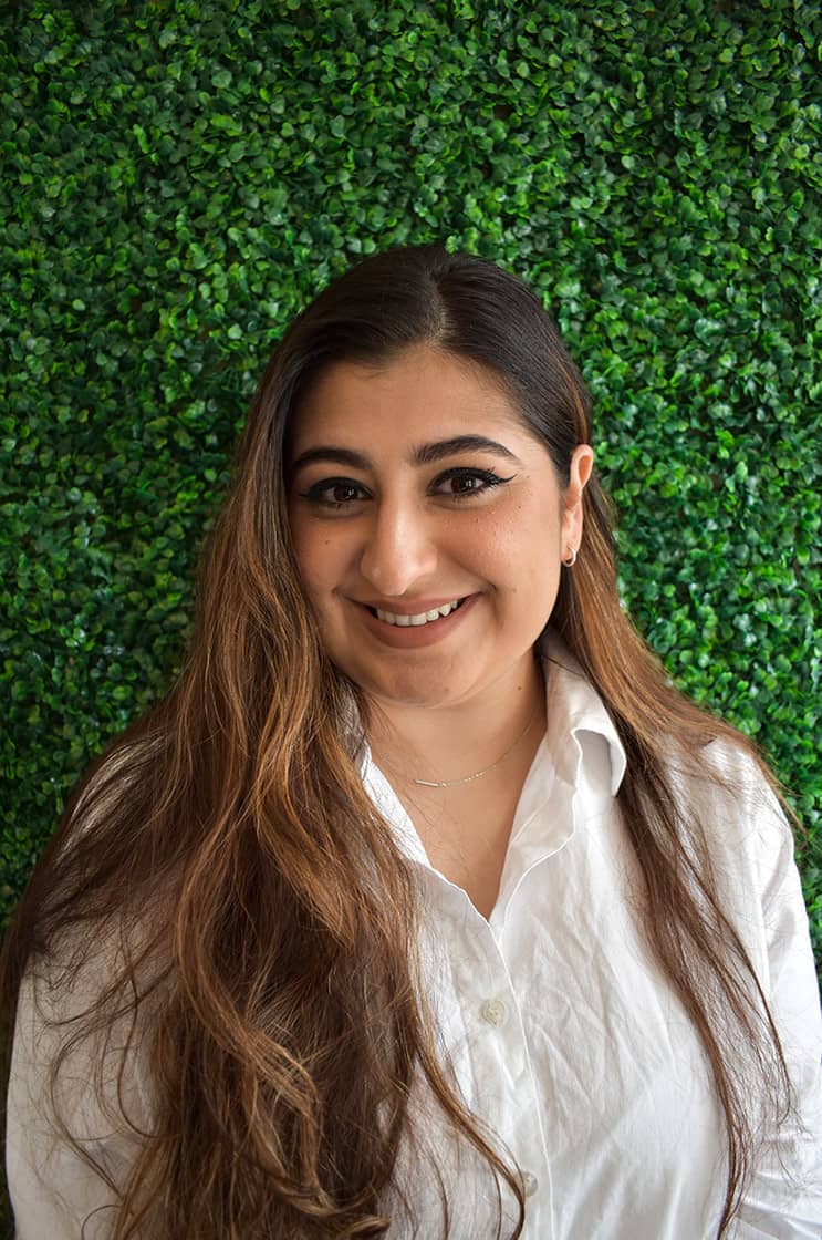 Kimya smiling in a white blouse against a verdant backdrop.