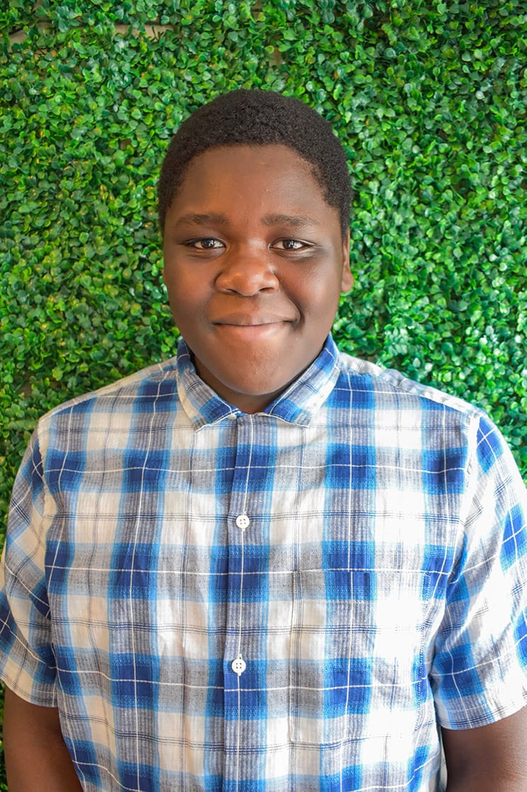 Adriel posing for the camera in a blue-checked button-up shirt.