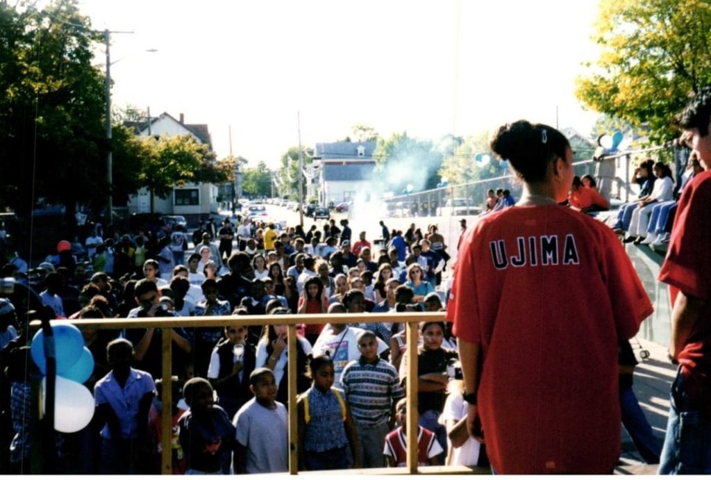 A crowd of youth gather on a sunny day, with balloons and barbecue smoke.