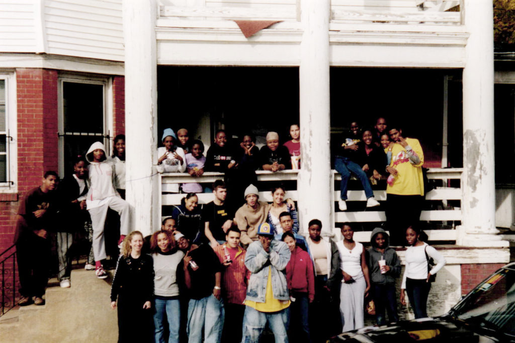 A large group of youth posing in front of an old brick building with white columns.