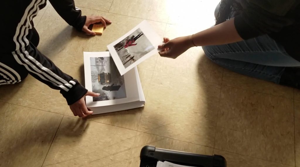 Two people crouched on the floor organizing photos of city streets covered in snow